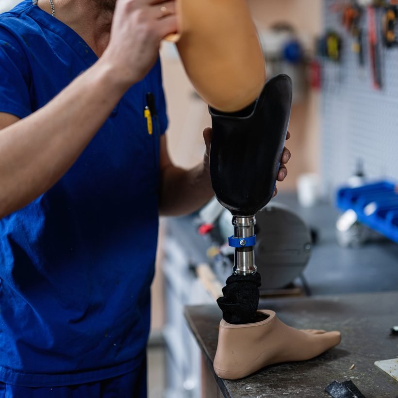 A skilled technician in blue scrubs assembles a prosthetic leg in a comprehensive workshop, showcasing the intricacies of modern prosthetic technology and medical craftsmanship.